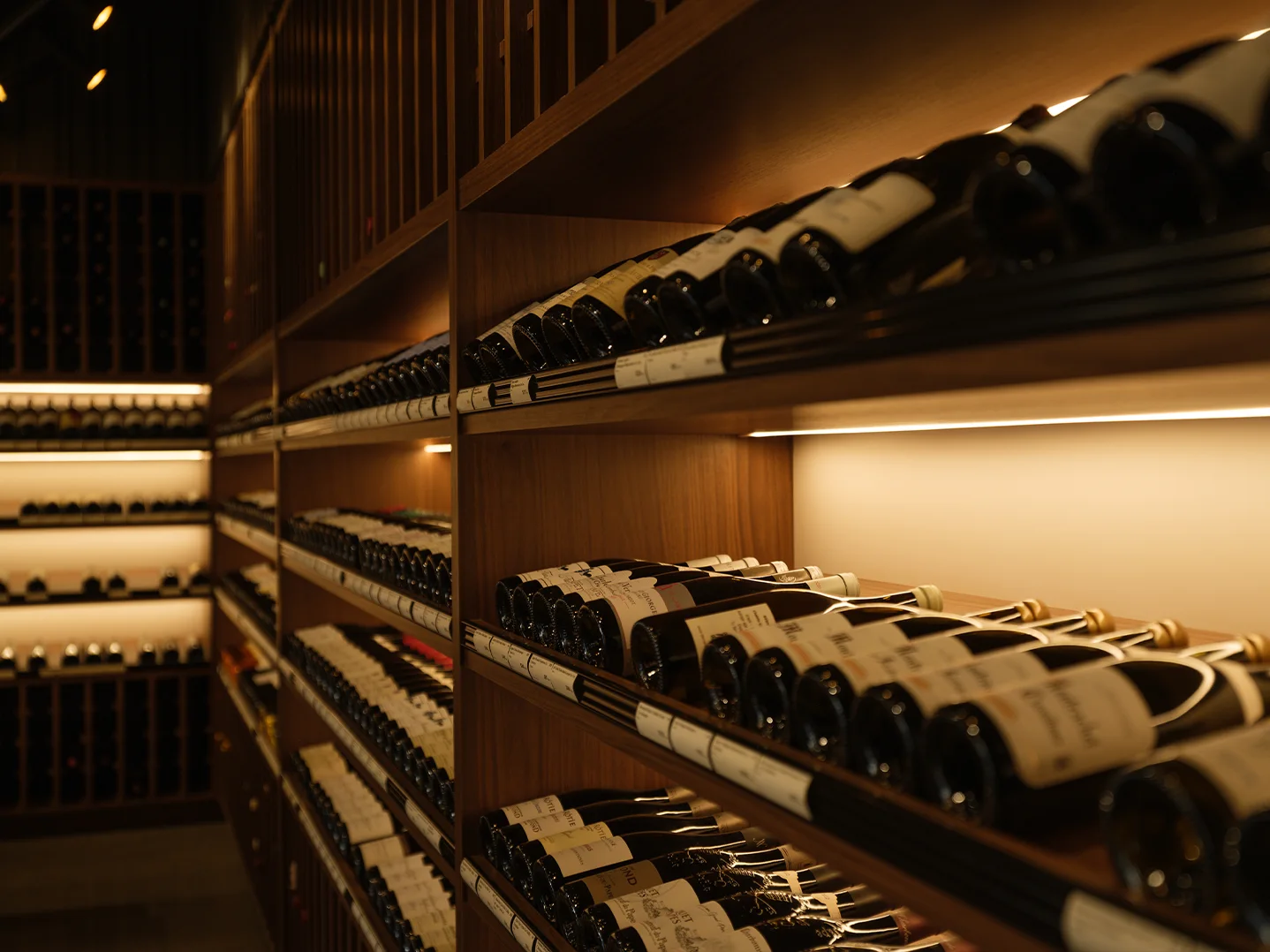 Side view of illuminated shelves of Burgundy bottles on their sides, with price labels along the shelf edges.