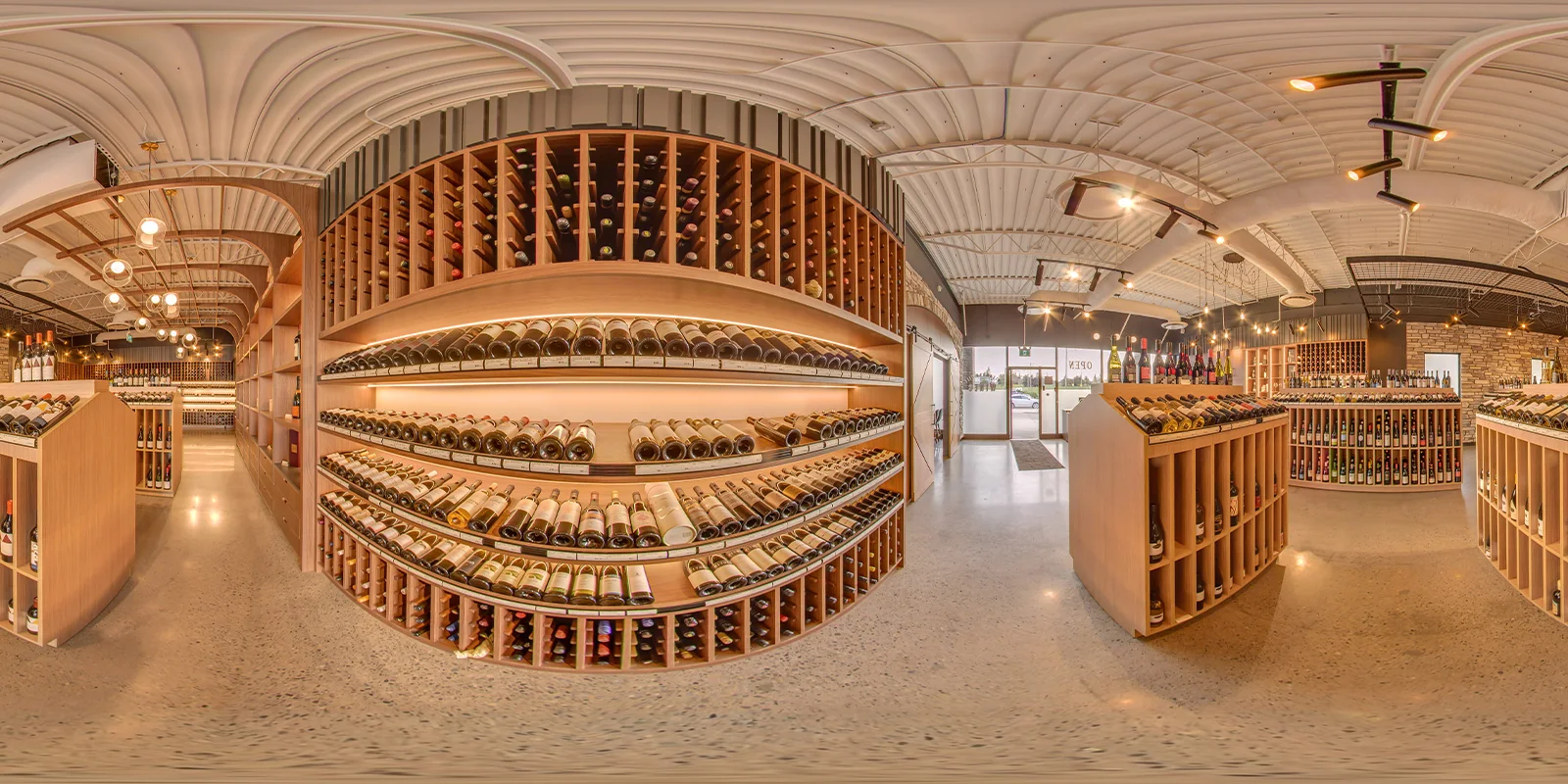 360° panorama of the retail floor with curved oak wine shelving, backlit bottle displays, and the front entrance in the distance.