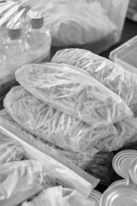 Plastic bags filled with pasta surrounded by canned goods and bottled water.