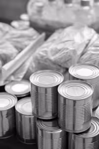 Stacked metal canned food with plastic bags of groceries in the background.