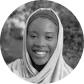 Portrait of a smiling woman wearing a headscarf outdoors with blurred greenery in the background.