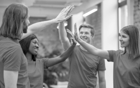 Group of four young adults in casual clothing giving each other high fives indoors.