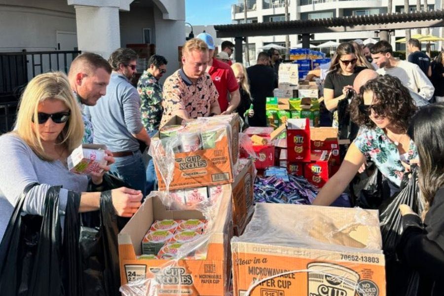 People picking up food supplies like Cup Noodles and Ritz crackers from a food distribution event outdoors under sunlight.