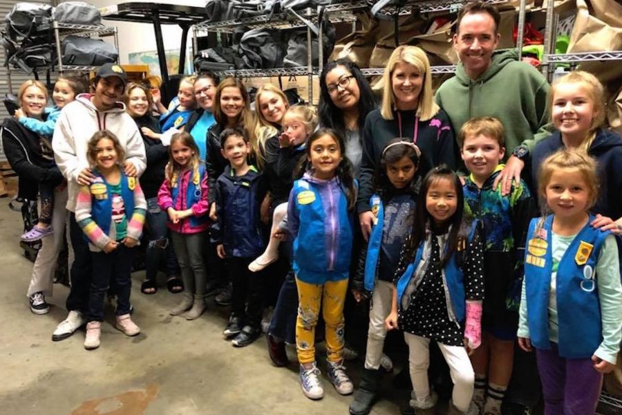 Group of diverse children and adults smiling indoors, with some children wearing blue Girl Scout vests.