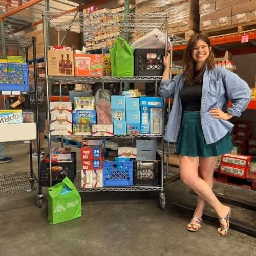 Smiling woman standing next to a metal shelf filled with grocery items in a warehouse aisle.