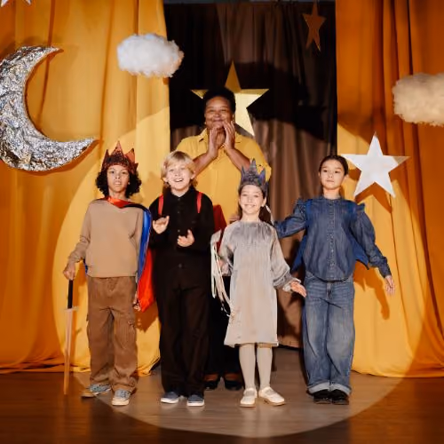 Four children and an adult on stage in costumes with stars, moon, and clouds backdrop.