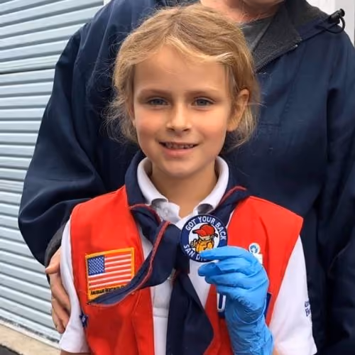 Young girl wearing a red vest and blue glove holds a patch saying 'Got Your Back San Diego'.
