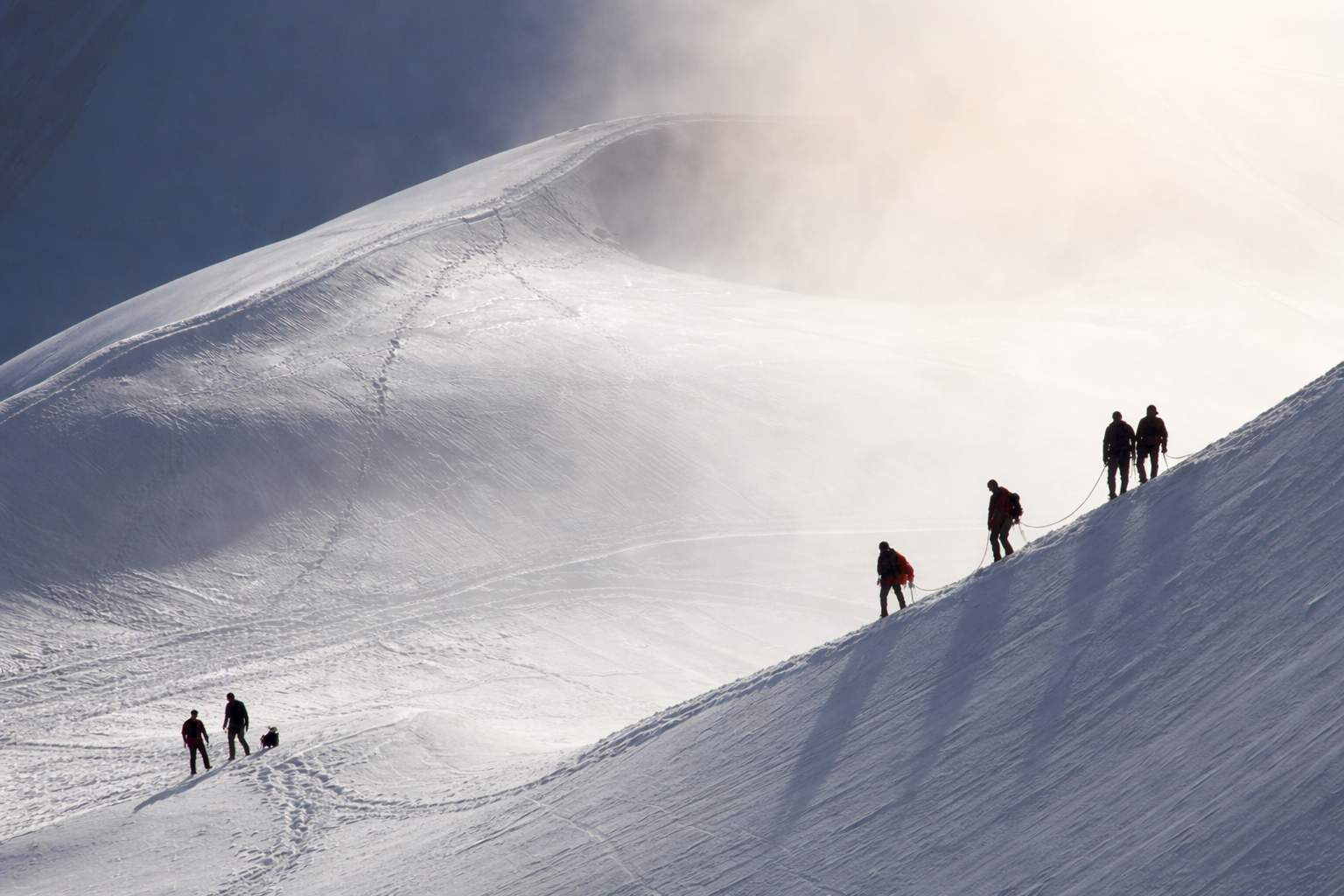 Bergsteiger in Seilschaft steigen einen schneebedeckten steilen Hang bei nebligem Licht hinauf.