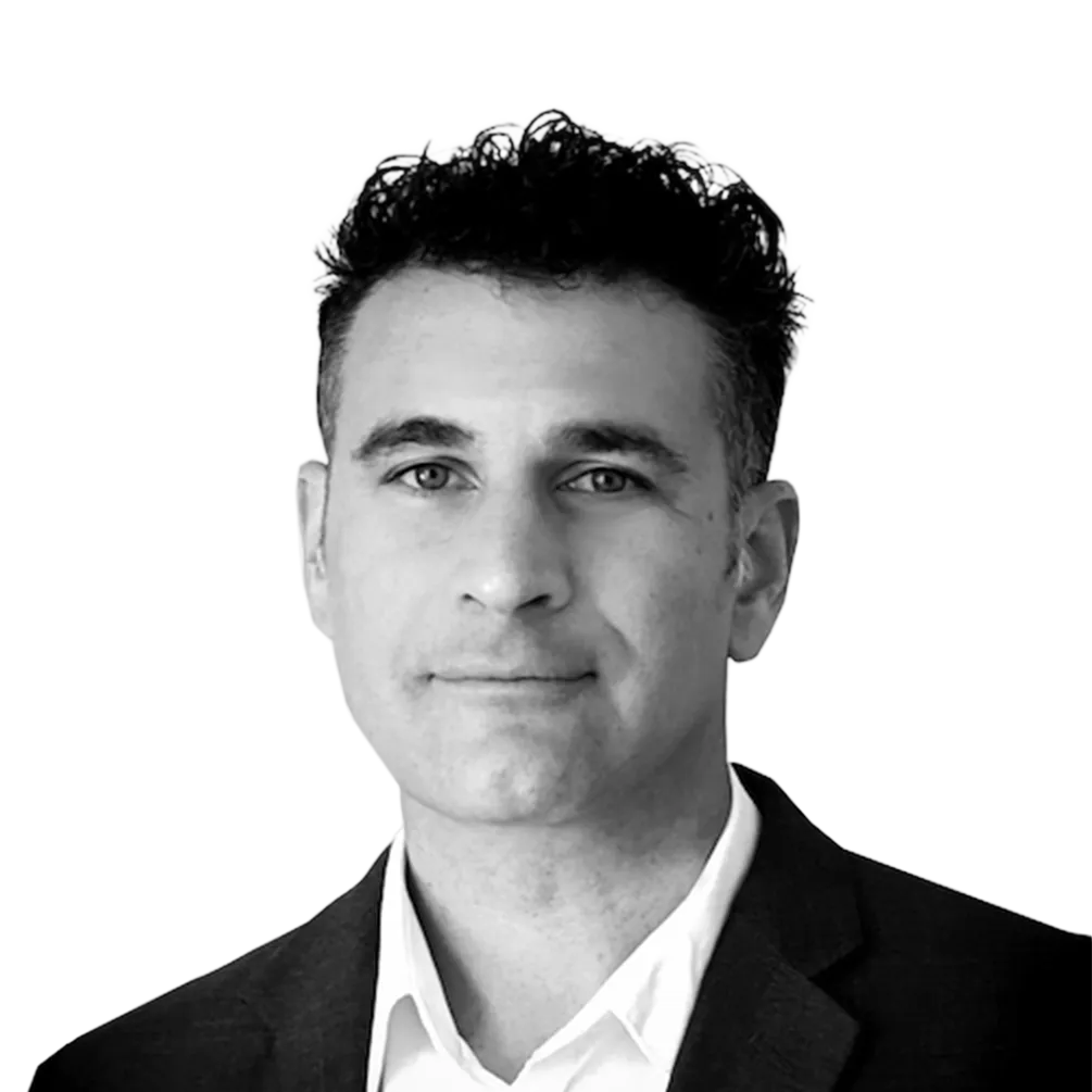 Black and white headshot of a man with short curly hair wearing a dark blazer and white shirt.