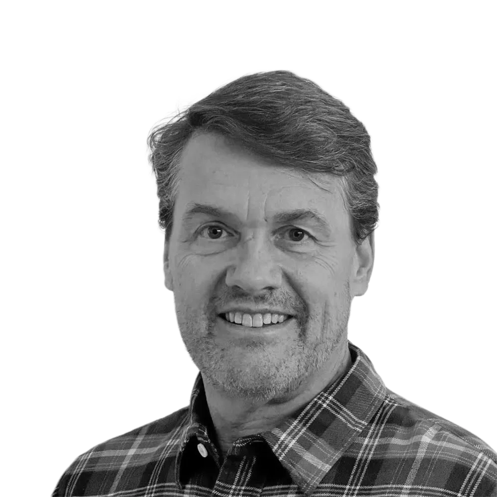 Middle-aged man with short hair and stubble smiling, wearing a checkered shirt.