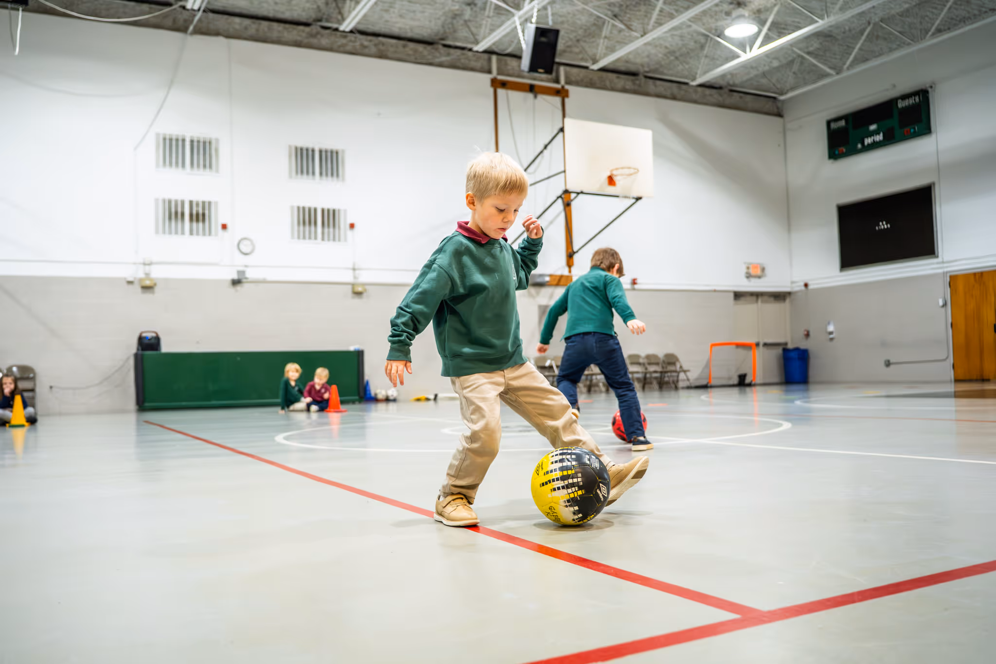 Six young school children sitting at a green cafeteria table eating lunch with lunchboxes and water bottles.