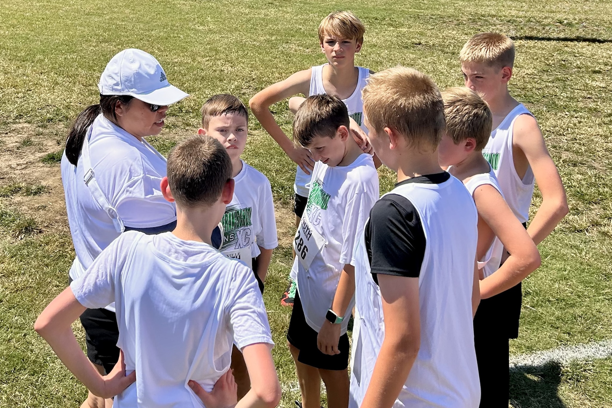 Children and a teacher sitting on a gym floor stretching their legs during a physical education class.