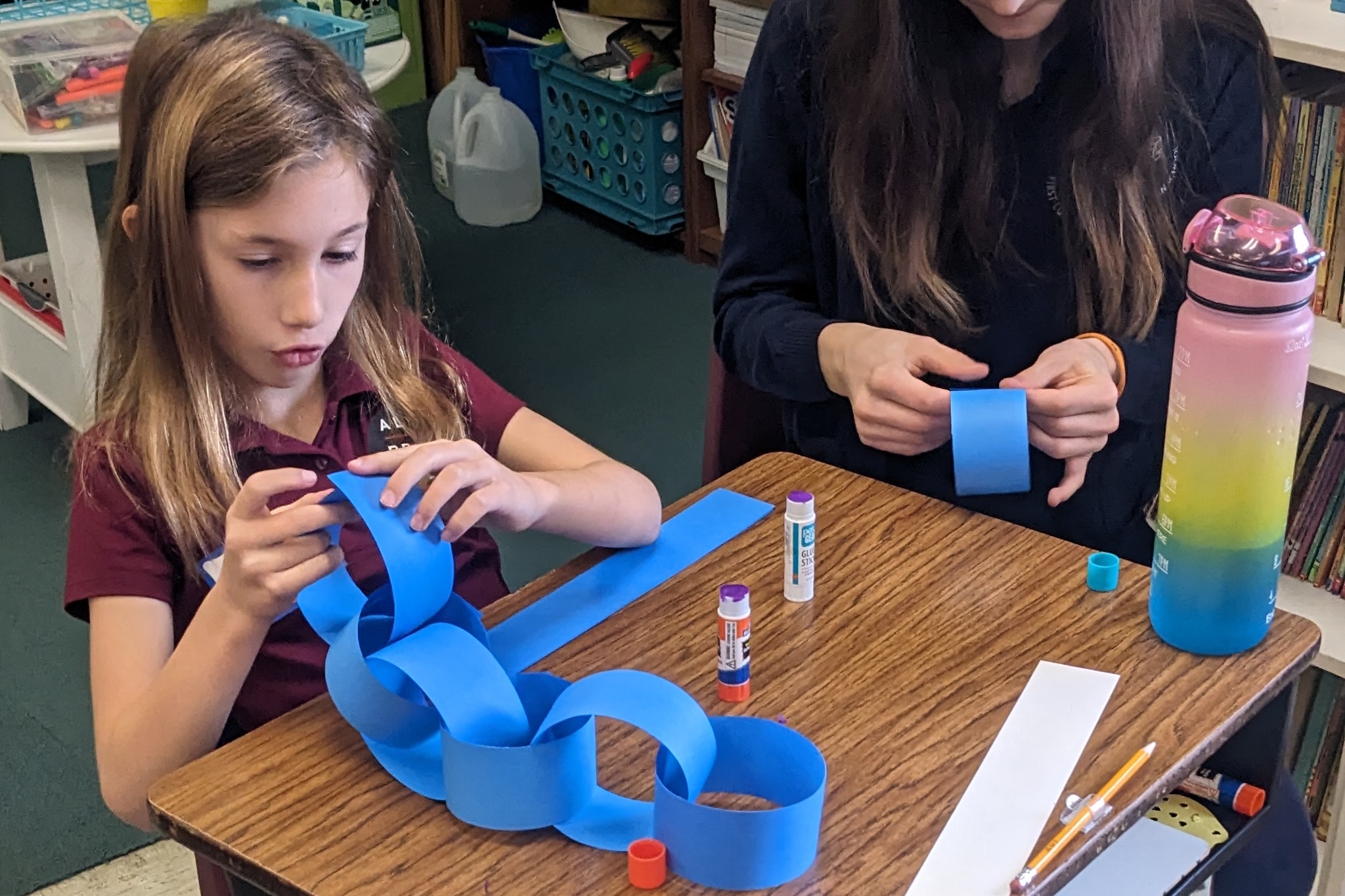 Group of young children sitting on a colorful rug in a classroom with hands raised eagerly.