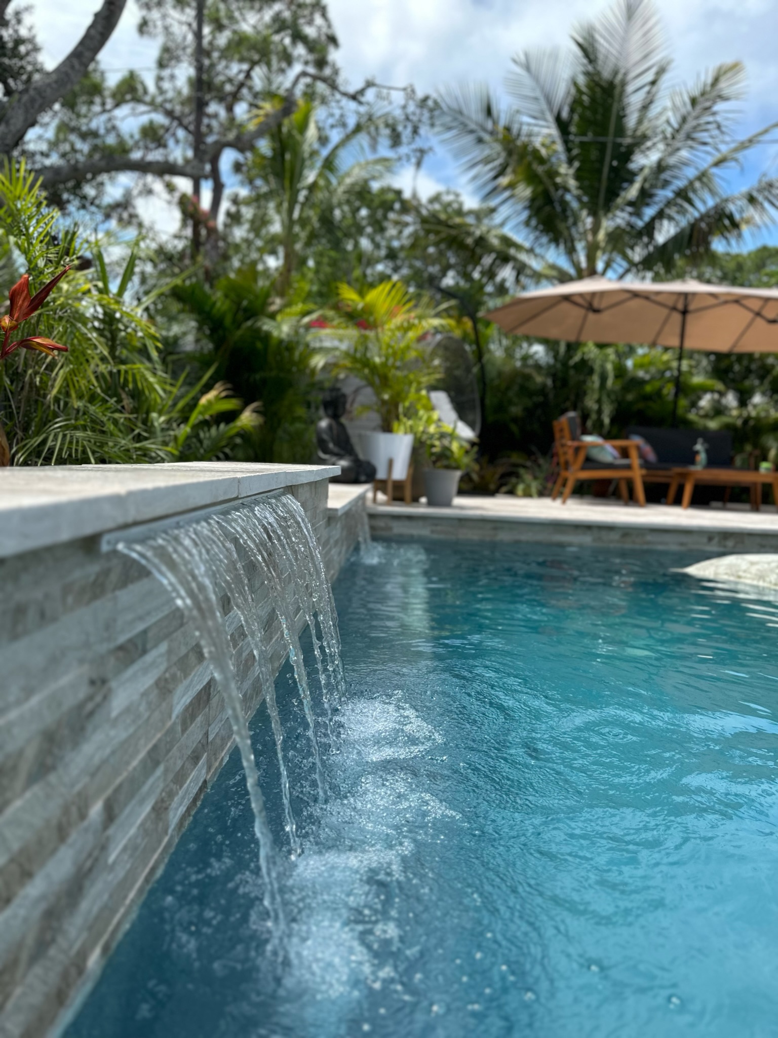 Water spilling from a raised tiled wall into a swimming pool.