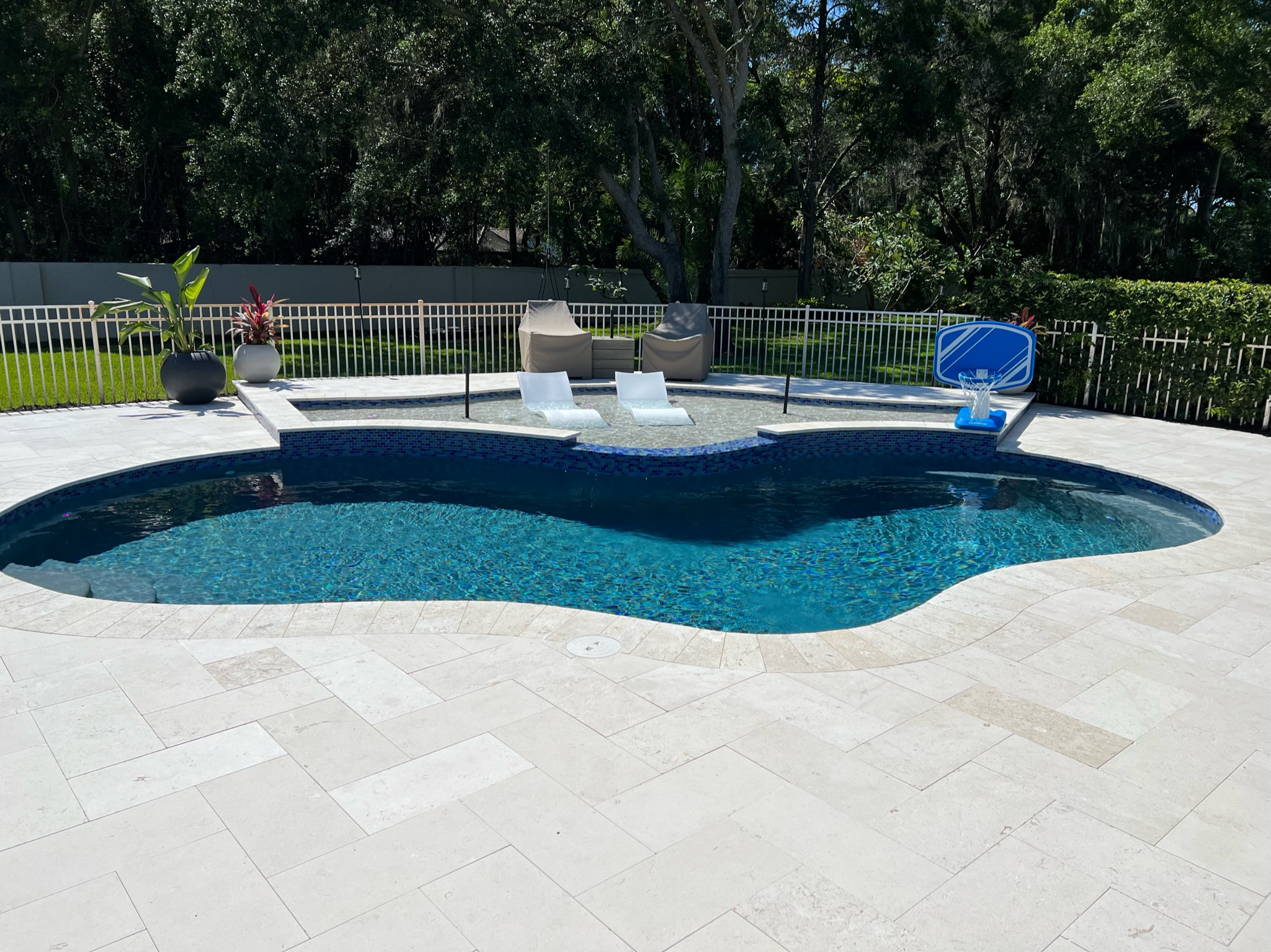 Finished swimming pool with a shallow shelf, two white loungers and curved paving.