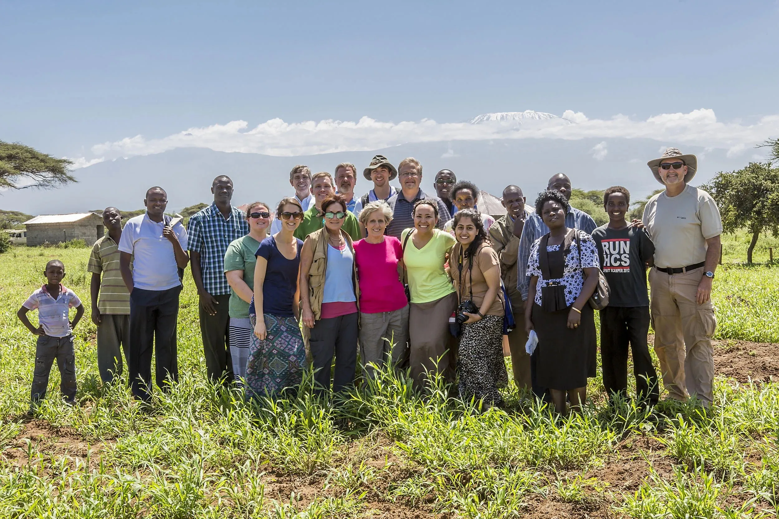 Group of diverse people standing in a green field with Mount Kilimanjaro in the background under a clear sky.