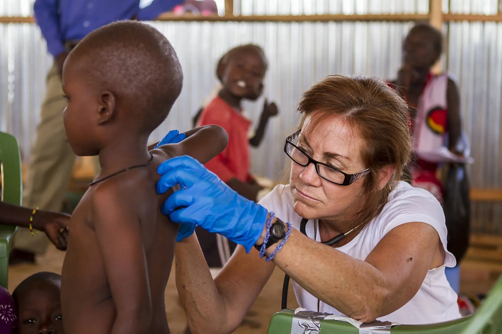 Healthcare worker wearing blue gloves examining the back of a young child in a clinic setting.