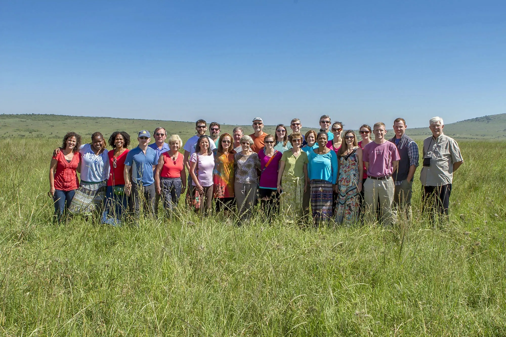 Group of diverse adults standing in a grassy field under a clear blue sky.