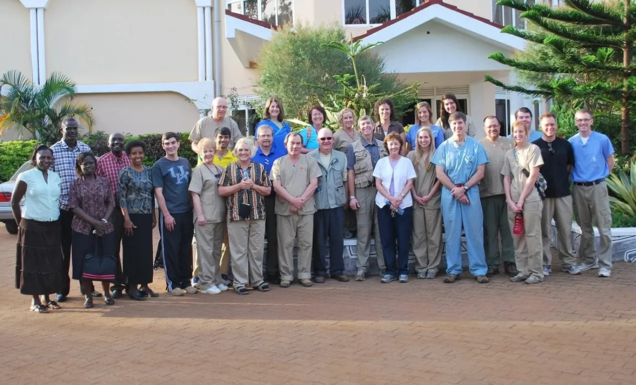 Group photo of diverse adults standing outdoors in front of a building with greenery.