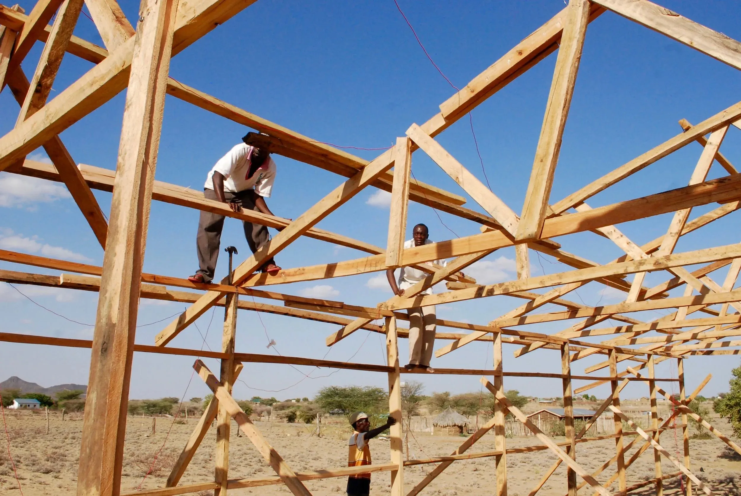 Three men constructing a wooden frame structure outdoors under a clear blue sky.