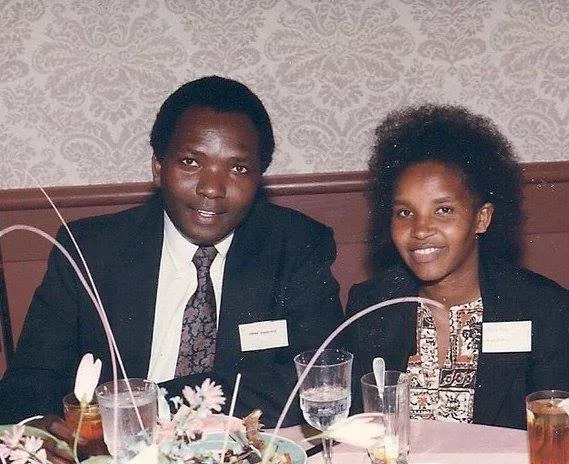 A man and a woman seated at a dining table with plates, glasses, and floral centerpiece, both smiling and dressed formally.