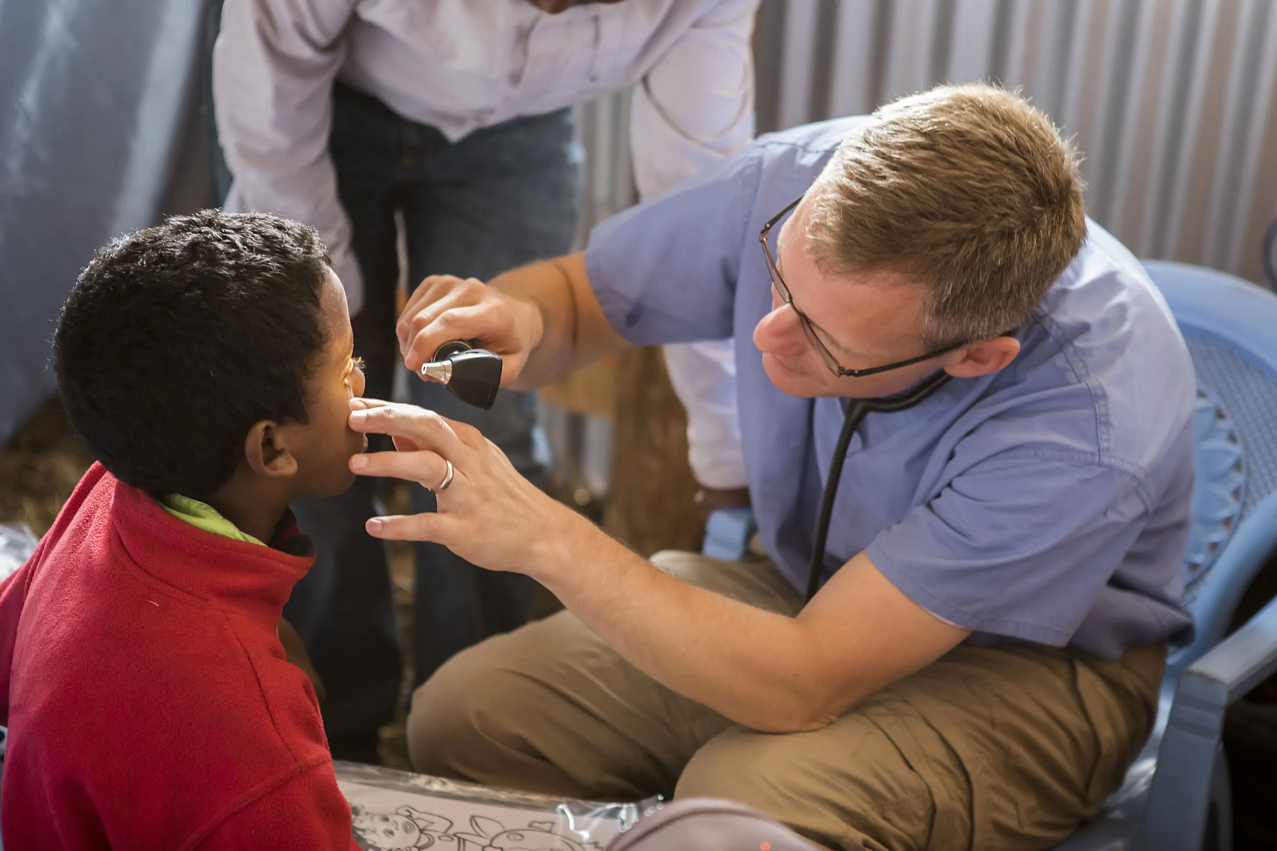 Healthcare professional in blue scrubs examining boy's eye with medical instrument.