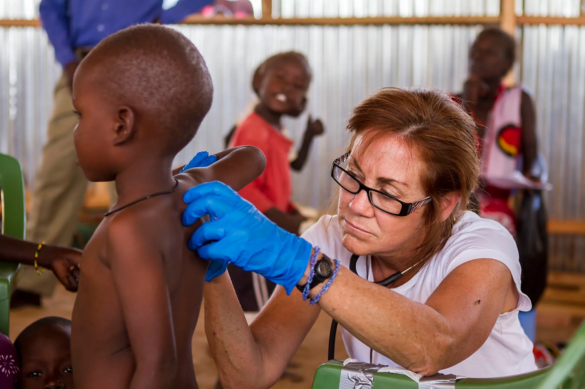 Female healthcare worker wearing blue gloves examines the back of a young child in a clinic setting.
