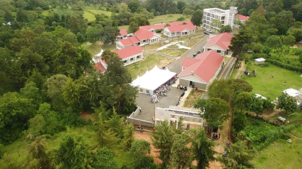 Aerial view of a compound with multiple red-roofed buildings surrounded by dense green trees and vegetation.