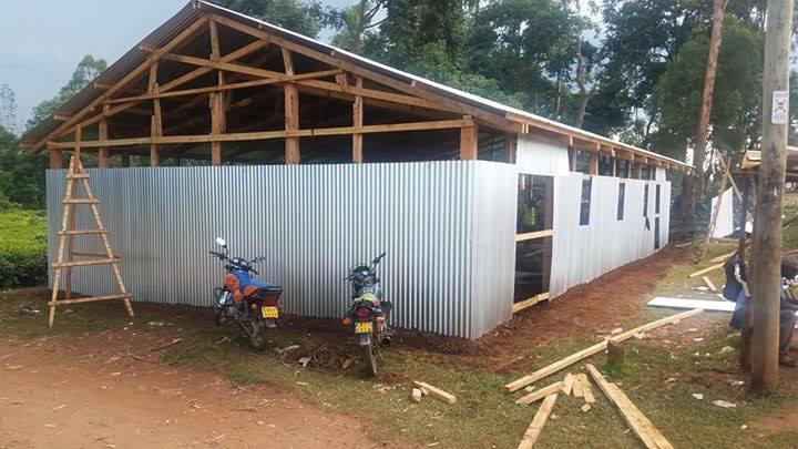 Partially constructed building with a wooden frame and corrugated metal siding, two motorcycles parked in front, and scattered wooden planks nearby.