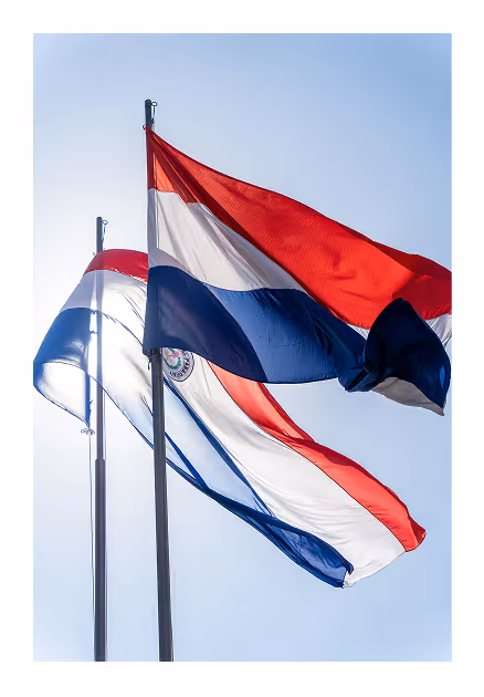 Dos banderas de Paraguay ondeando con el cielo azul de fondo.