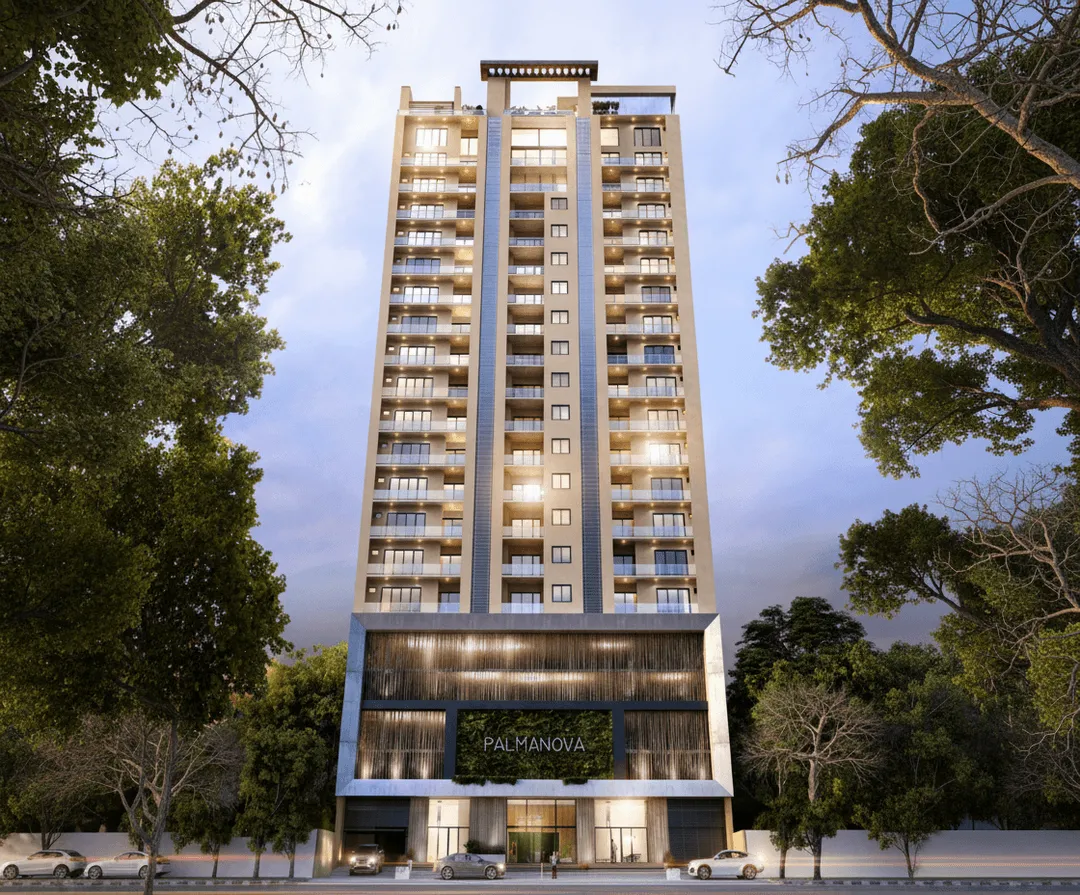 Edificio alto y moderno llamado Palmanova rodeado de árboles con luces encendidas al atardecer.