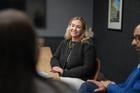 A woman sits at a table, smiling, during a meeting with two other people in a conference room.
