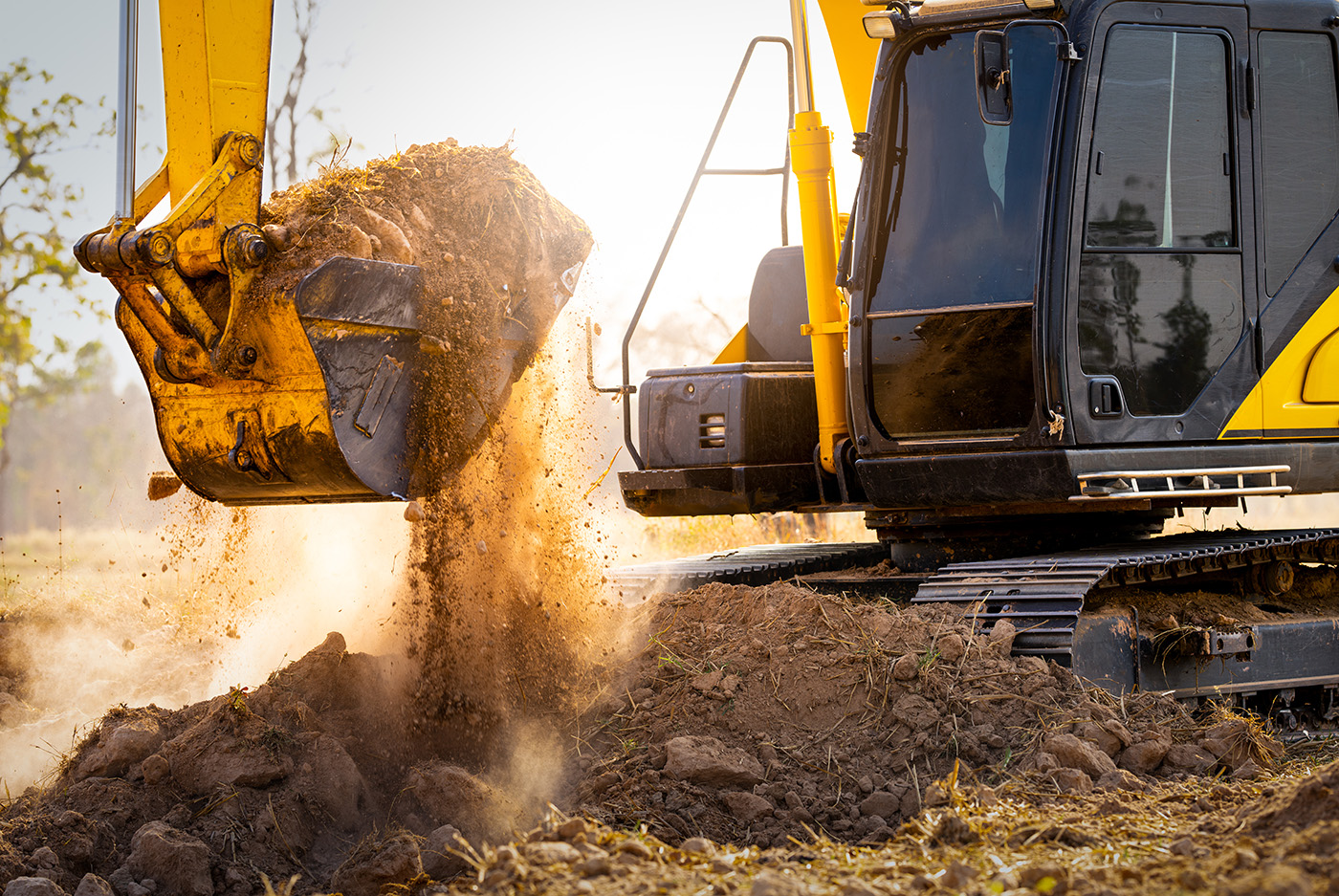 Yellow excavator dumping a bucket of dirt at a construction site.