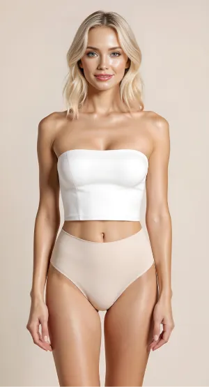 Blonde woman with loose waves wearing a white strapless crop top and high-waisted nude underwear standing against a beige background.