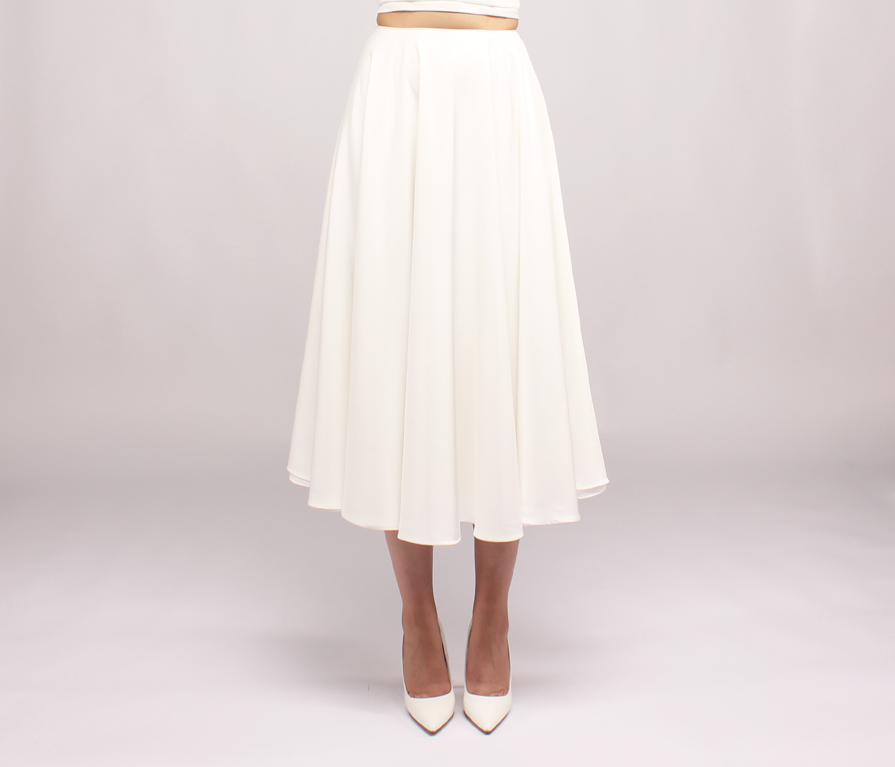 Person wearing a white midi skirt and matching white pointed-toe high heels against a plain background.