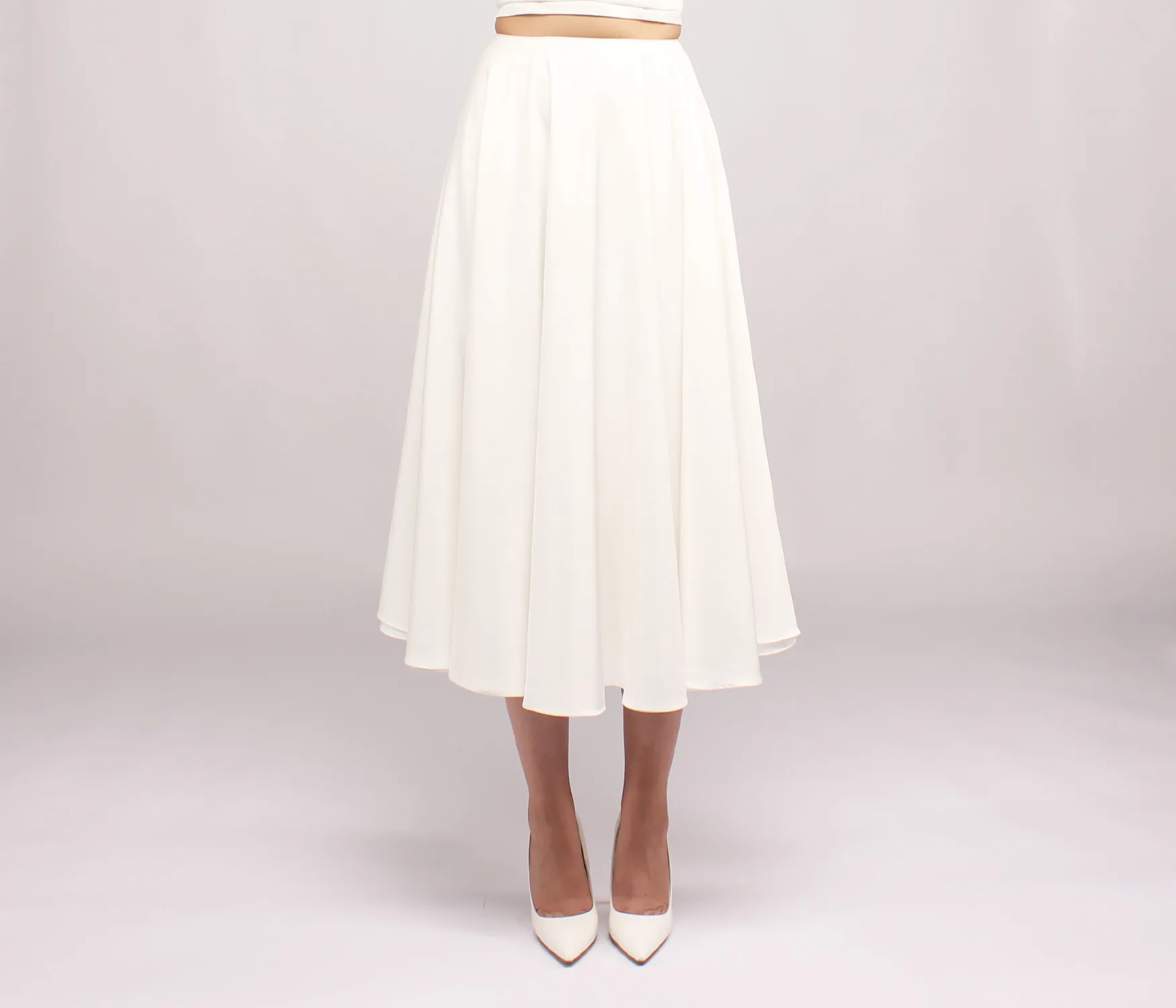 Person wearing a white midi skirt and matching white pointed-toe high heels against a plain background.