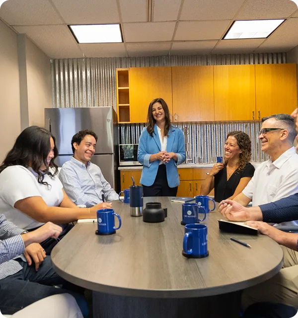 Pamela Garrett leading a team meeting with staff gathered around a table in the office