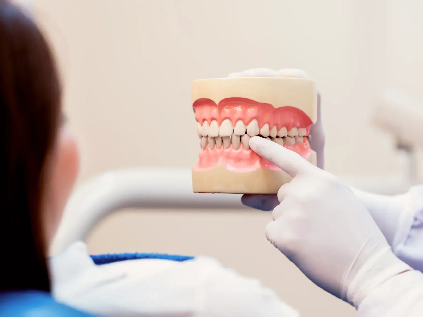 Dentist wearing white gloves pointing to a dental model held in front of a patient.