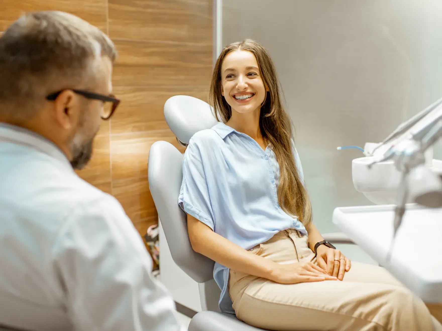 Smiling young woman sitting in a dental chair talking with a male dentist in a modern dental office.