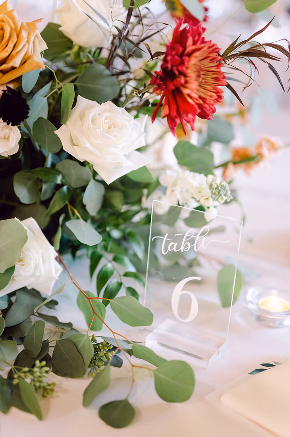 Table 6 sign surrounded by white, orange, and red flowers with green foliage on a white tablecloth.