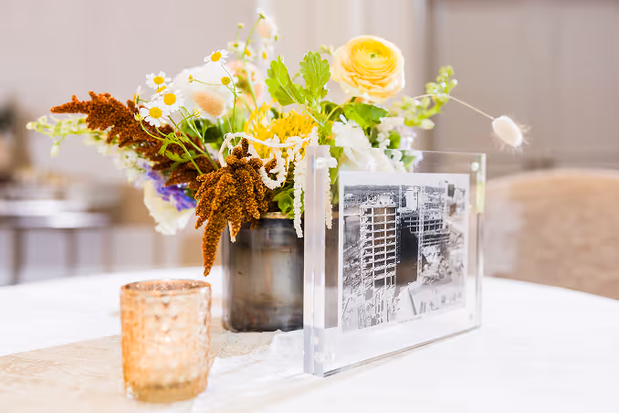 Decorative table arrangement with mixed flowers in a vase alongside a framed black and white photo and a textured glass candle holder.
