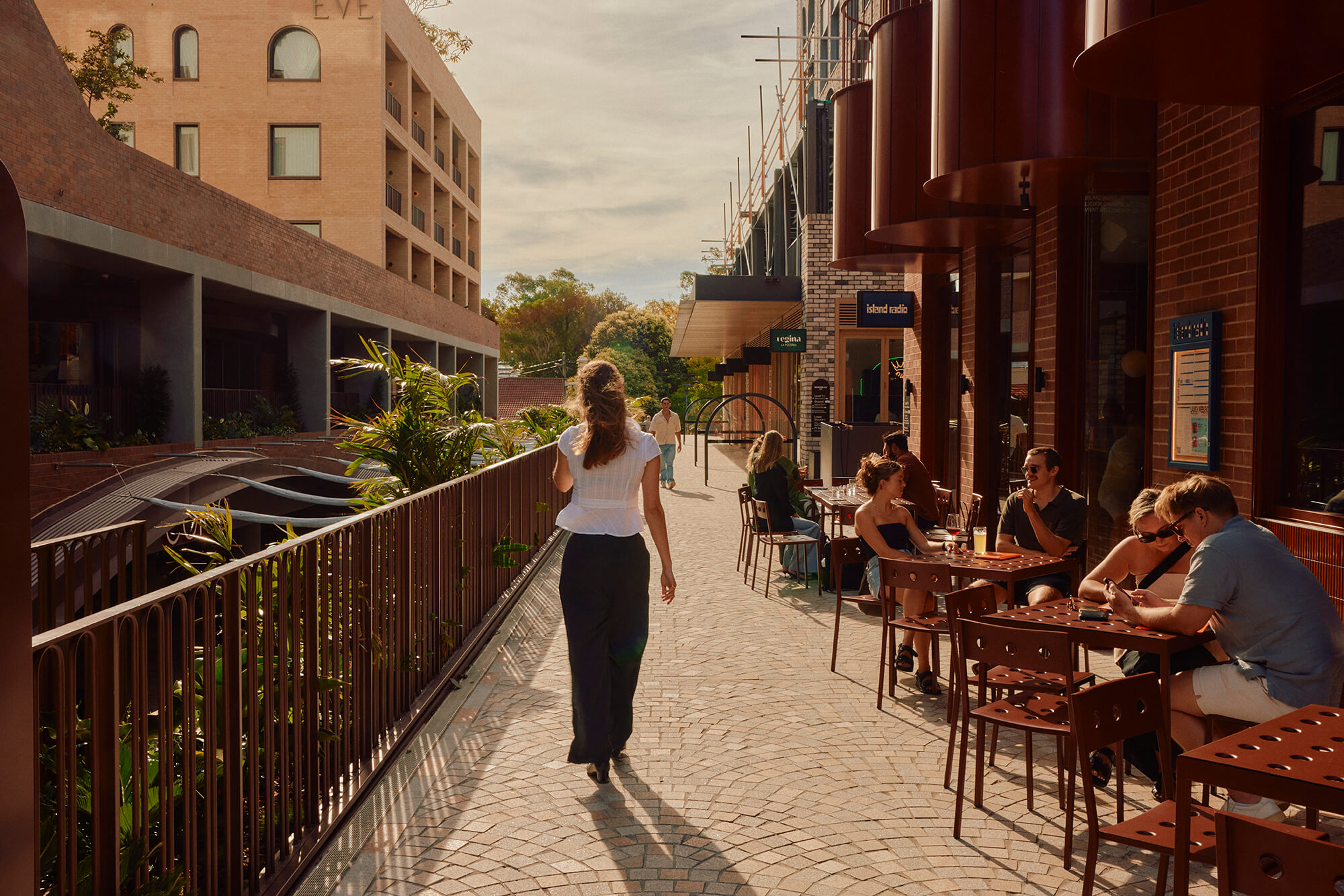 Woman walking along a path beside a restaurant in an urban village setting.
