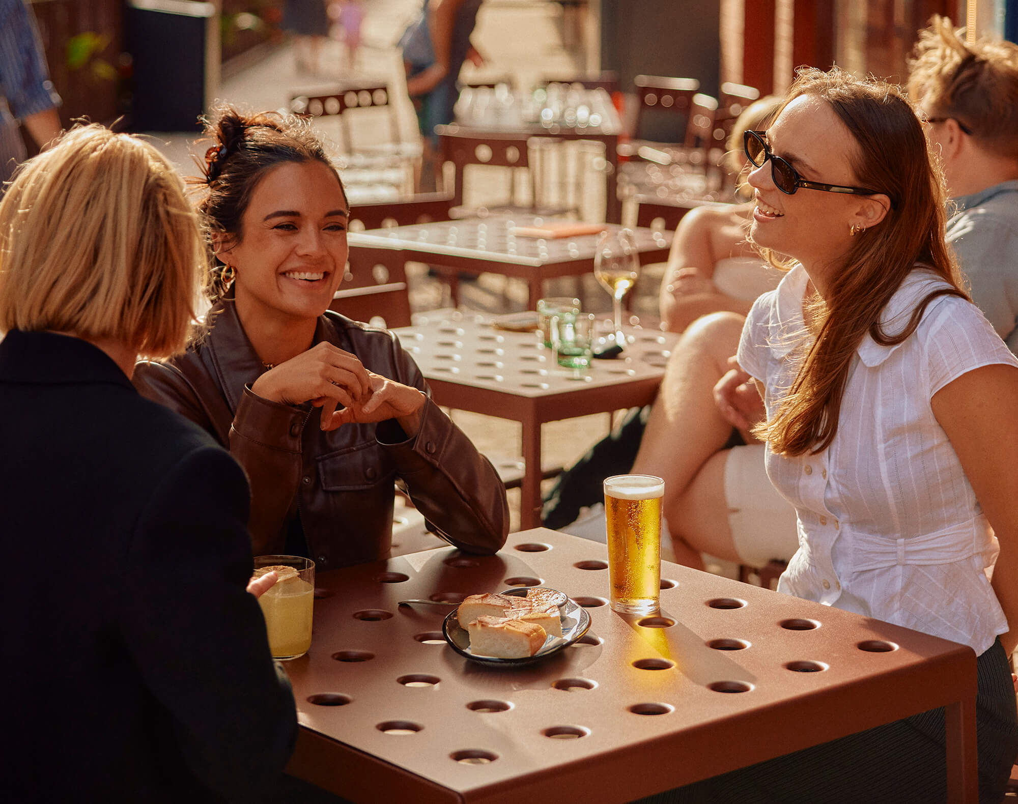 People enjoying food and drinks together at an outdoor restaurant in an urban village setting.