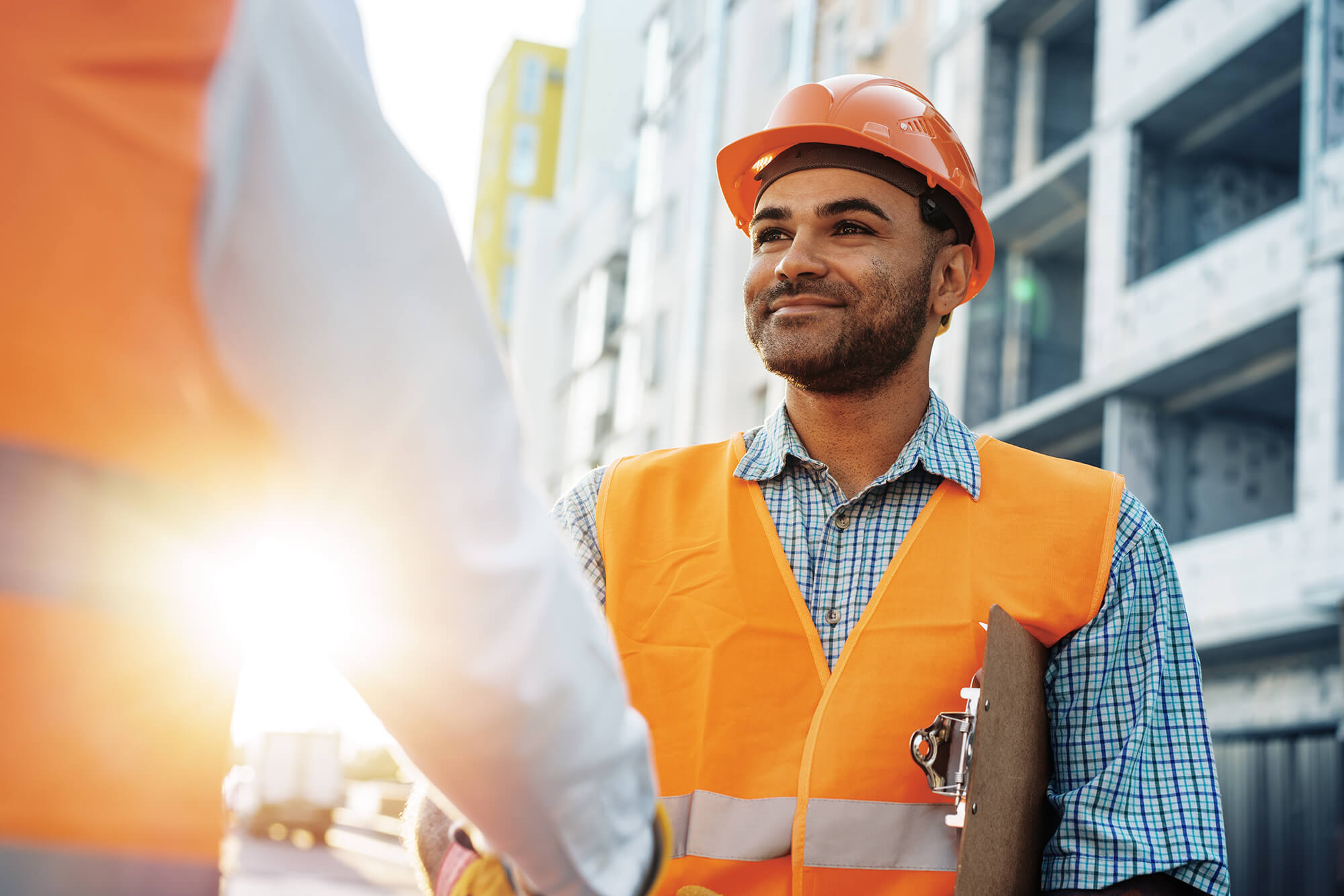 Construction workers shaking hands on-site with buildings in the background.