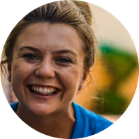 Close-up of a smiling woman with blonde hair and a blue shirt in an outdoor setting.