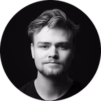 Black and white portrait of a young man with light hair and a short beard against a dark background.