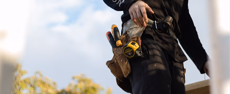 Construction worker wearing a tool belt with various tools including a measuring tape and screwdrivers.