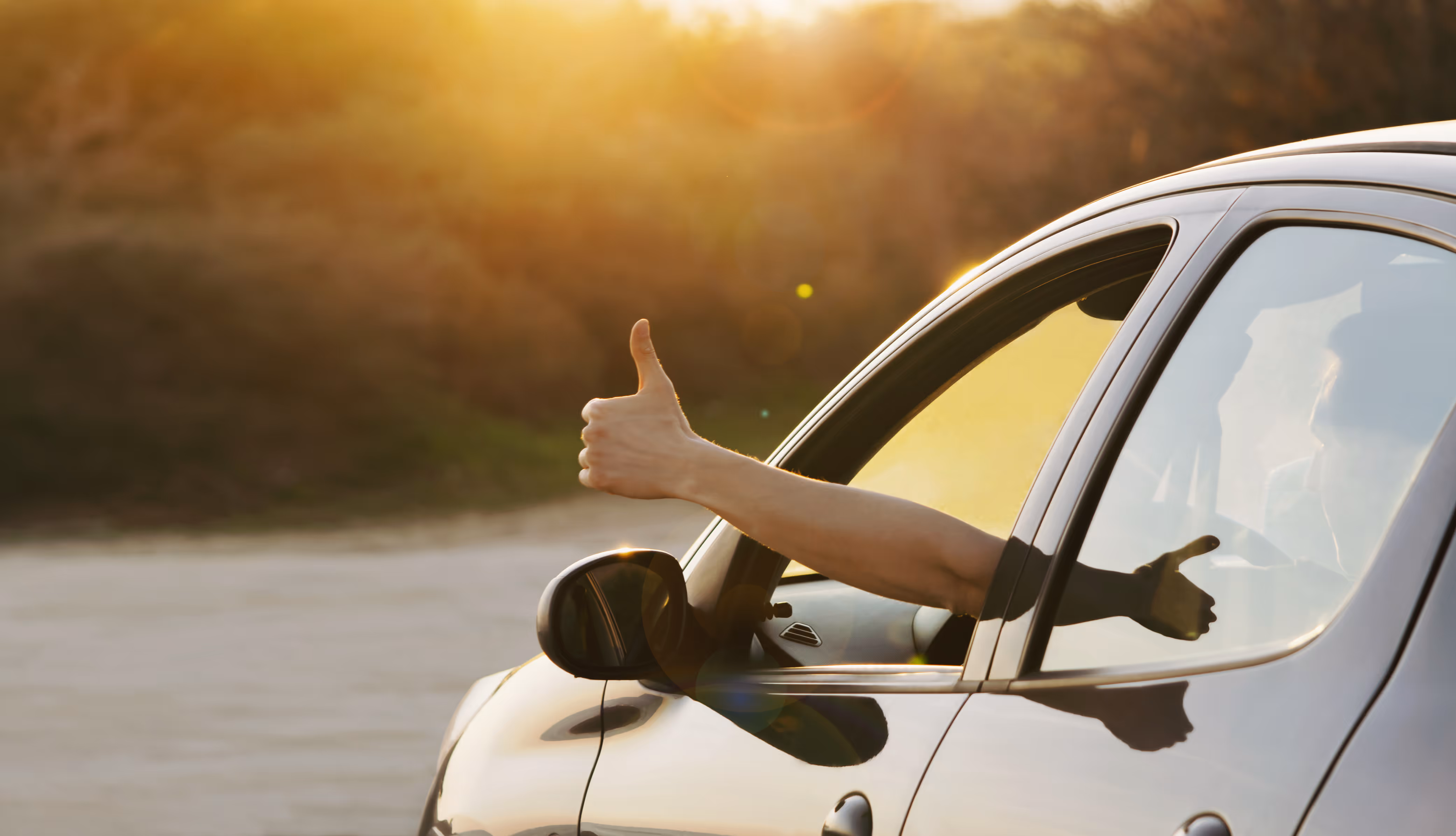 Person inside car giving a thumbs-up through the open window at sunset, RentUFS.