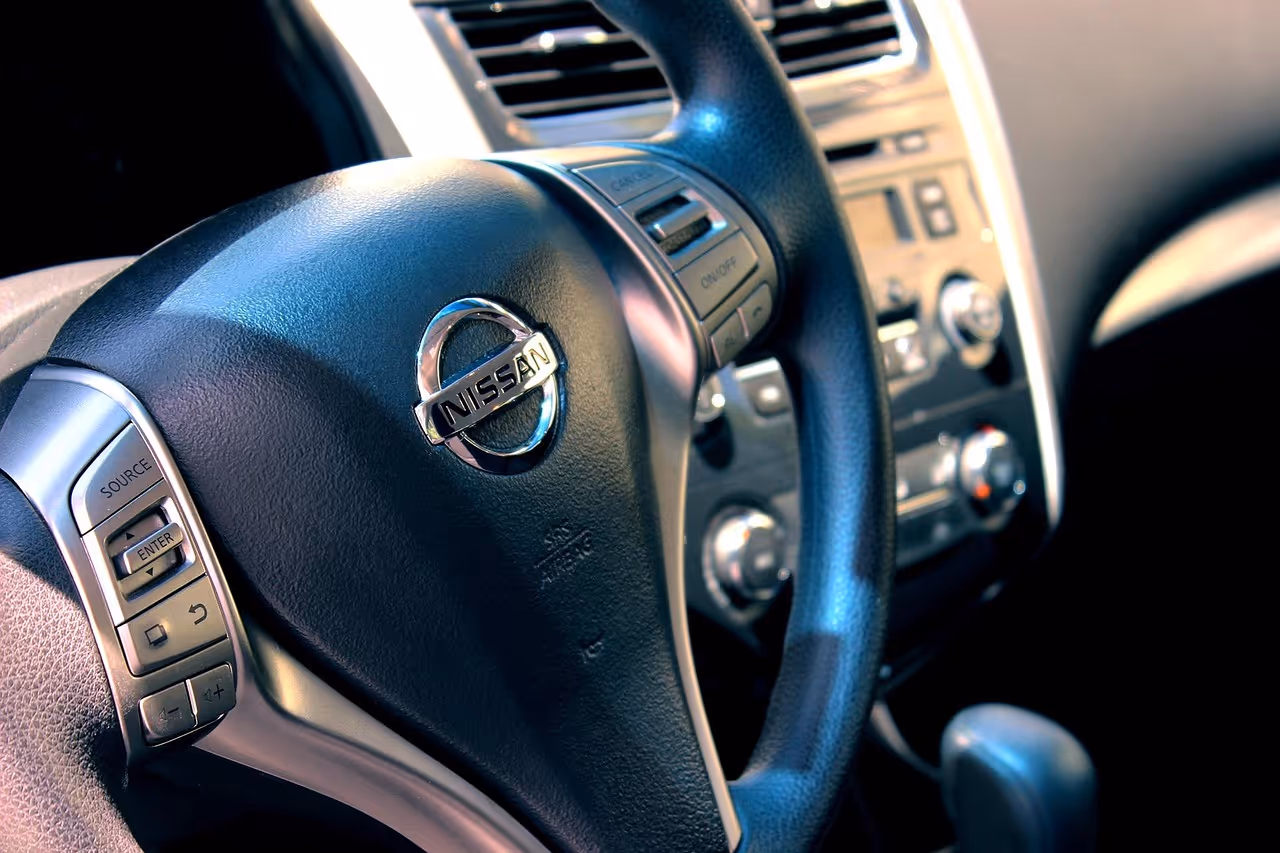 Close-up of a Nissan car steering wheel with control buttons and dashboard in background, RentUFS.