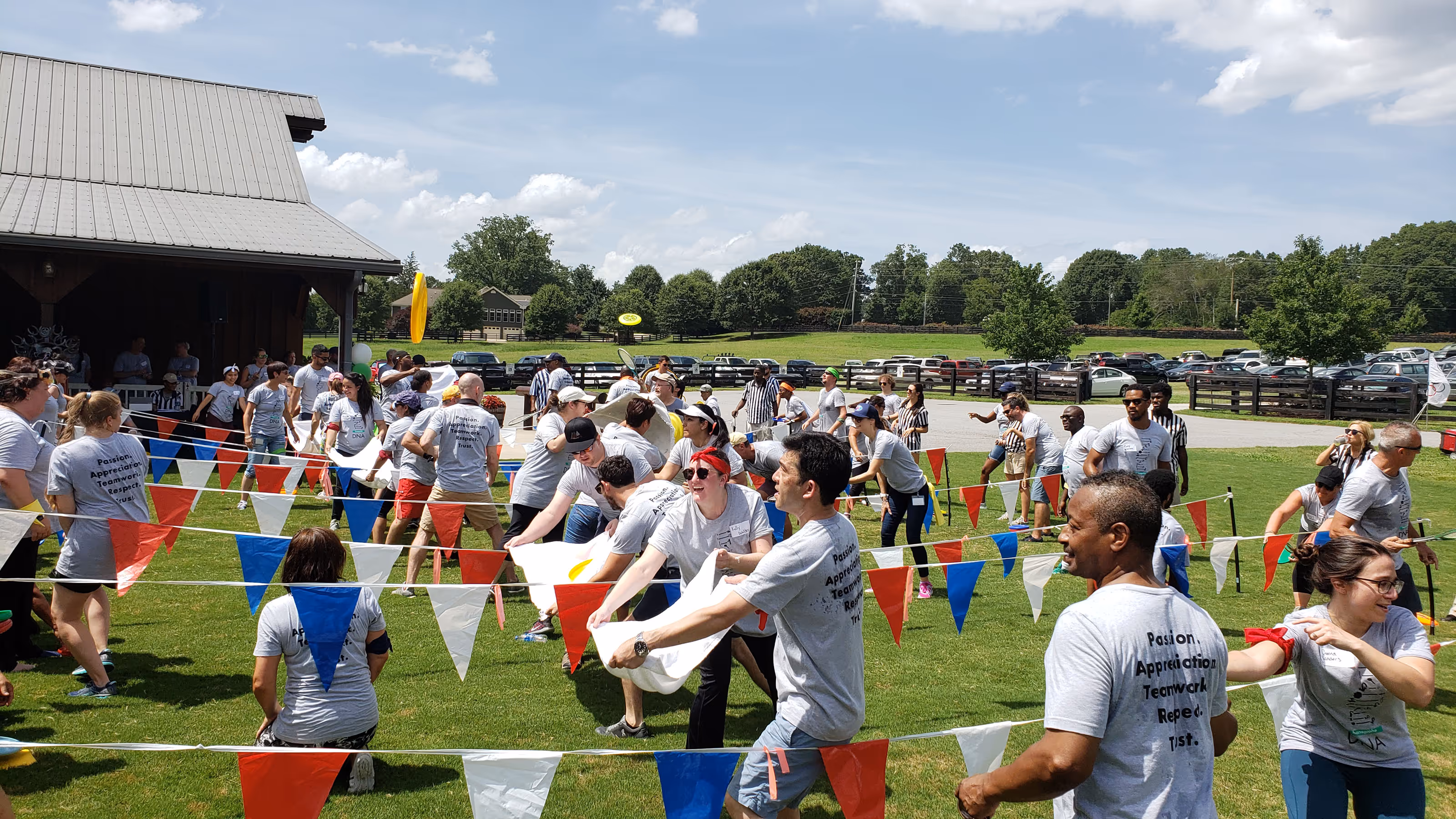 Employees taking part in an outdoor corporate team-building competition with colorful flags and facilitators.